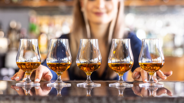 A lady presenting 5 snifters of whiskey on the bar counter