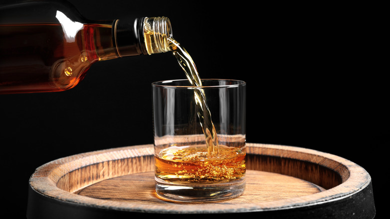 Pouring bourbon into a rocks glass on a barrel