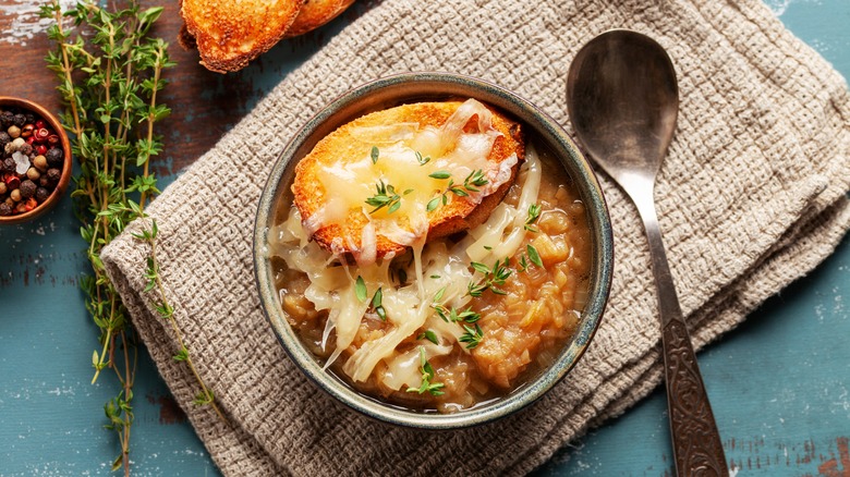 French onion soup in a bowl on a placemat with peppercorns and thyme next to it