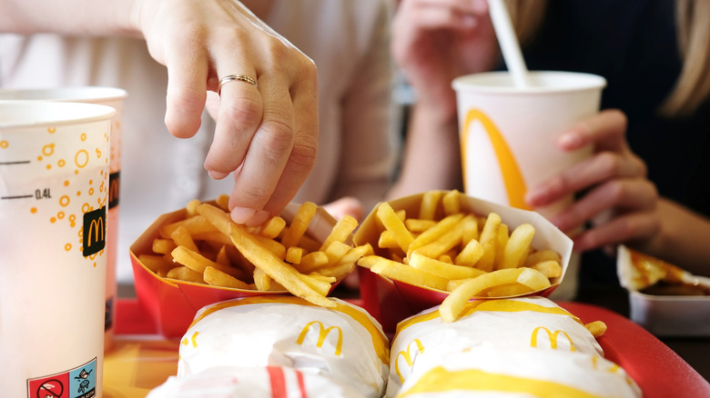 A hand reaches into a container of McDonald's french fries on a tray also containing other McDonald's food