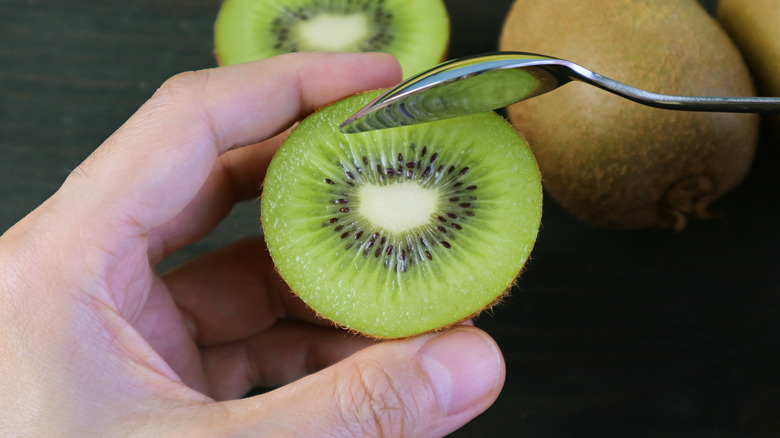 hand holding halved kiwi fruit with spoon