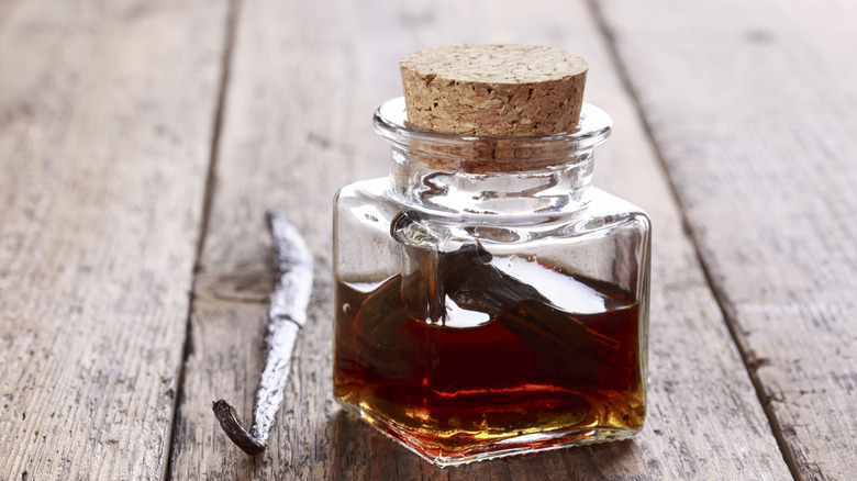 A corked bottle of vanilla extract next to vanilla beans