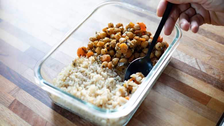 Glass bowl, half-filled with plain rice, half-filled with cooked chickpeas and vegetables. A person reaching into the dish with a spoon.