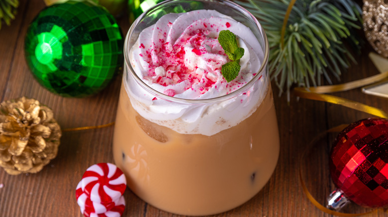 Iced latte topped with crushed candy canes surrounded by Christmas tree ornaments