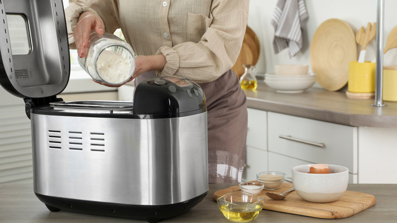 A baker adds flour to a bread machine