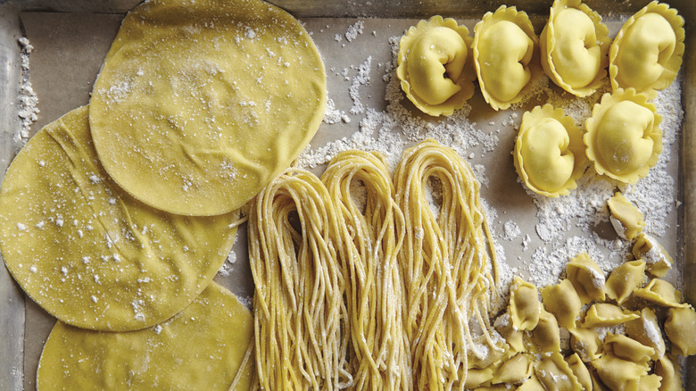 A tray full of different pasta doughs, including spaghetti, tortellini, and unfilled ravioli