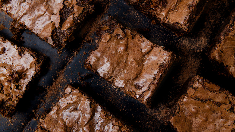 Some freshly made chocolate brownie squares on a black background.