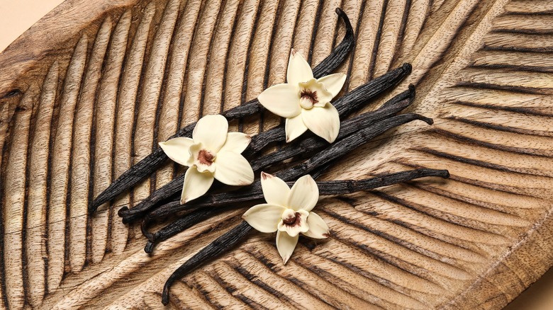 Vanilla bean pods and flowers on a wooden plate