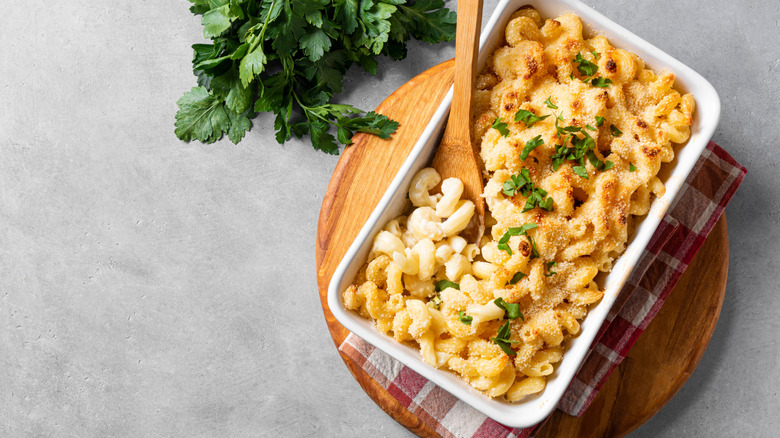 A baking dish filled with mac and cheese has a wood spoon inside