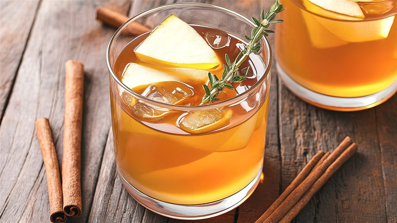 Glass of apple cider with ice, apples, and herbs