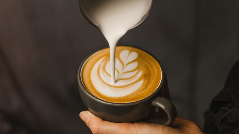 A barista pouring milk in coffee