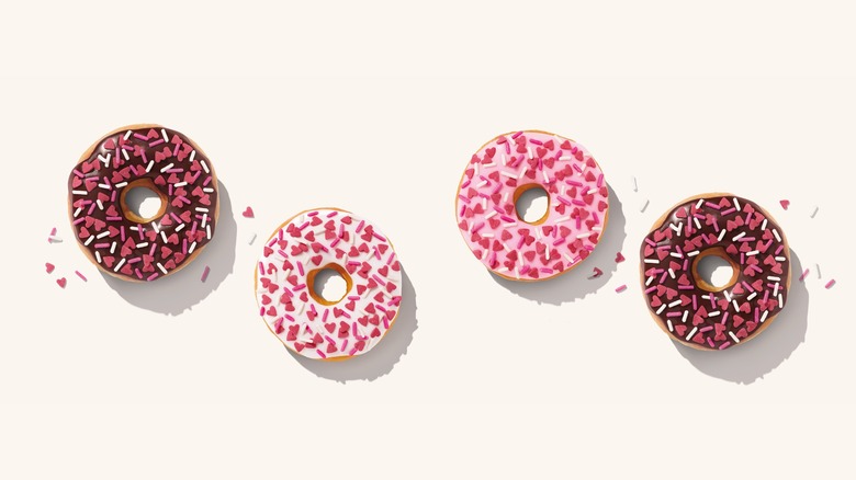 Four Dunkin' donuts in various colors, themed for Valentine's Day with pink heart sprinkles