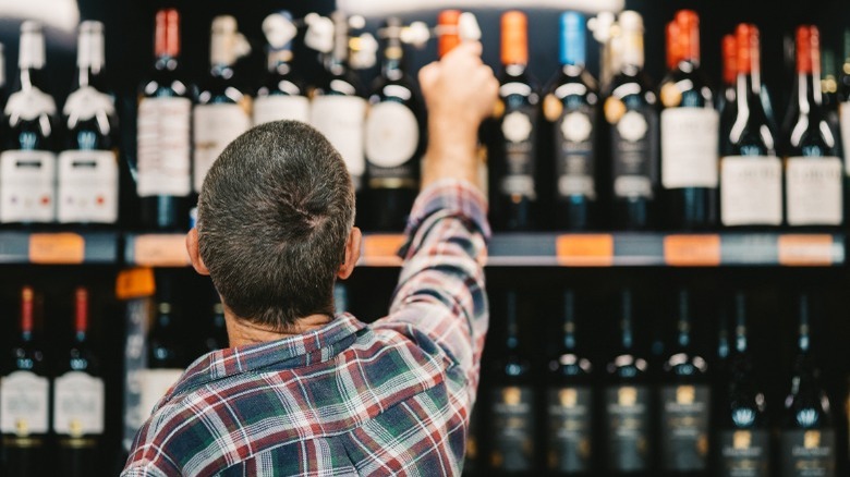 Man reaching for a bottle of wine on a shelf 