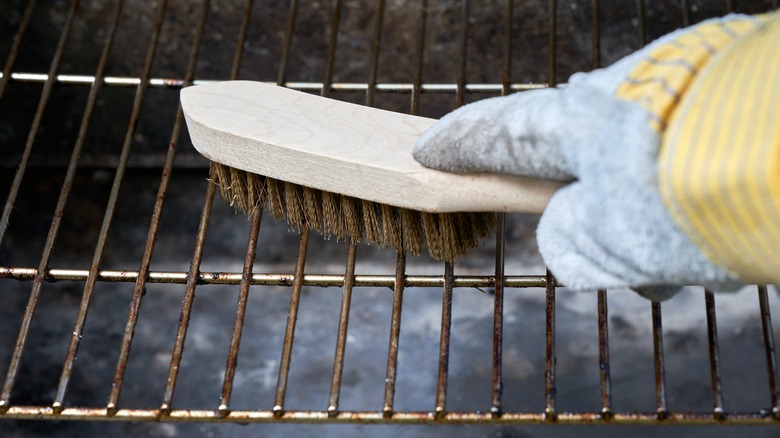 Gloves hand scrubbing dirty grill grates with a bristled brush