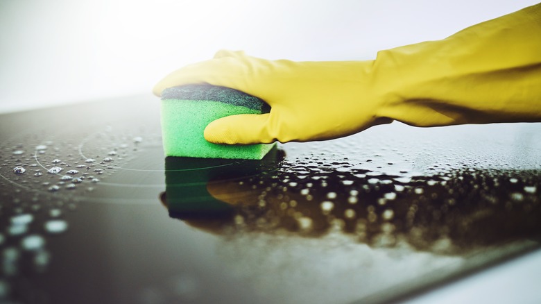 Yellow gloves hand scrubbing metal surface with green sponge