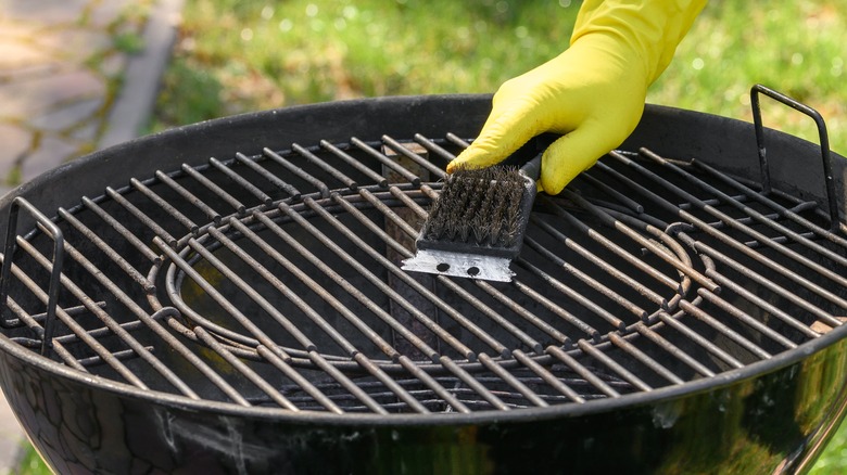 Yellow gloved hand scraping a grill grate with a scrub brush