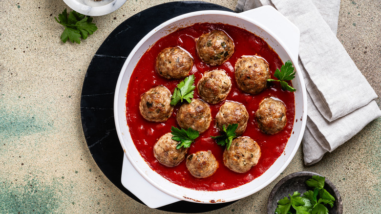 Several meatballs in a white pot full of tomato sauce with green herbs