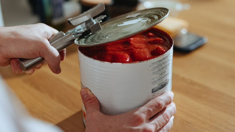 Person opening canned tomatoes