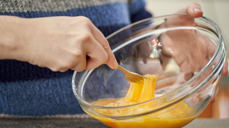 A baker whips an egg mixture with a fork in a glass mixing bowl