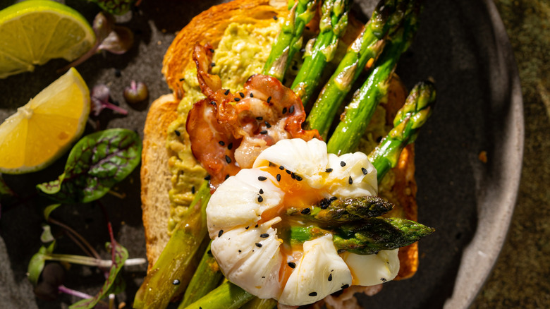 A poached egg on toast with grilled asparagus and bacon.