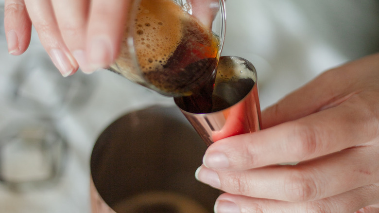 hands pouring espresso into cocktail shaker