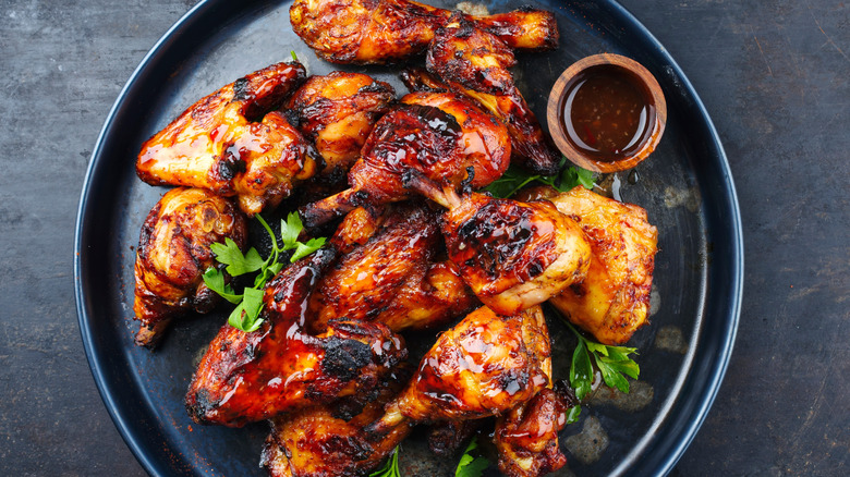 A plate of barbecue chicken with a ramekin of barbecue sauce on top, topped with fresh herbs.