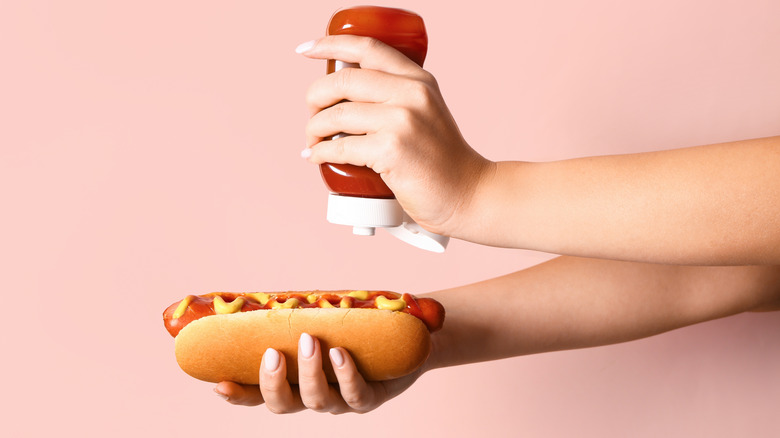 Hands holding a hot dog and a container of ketchup