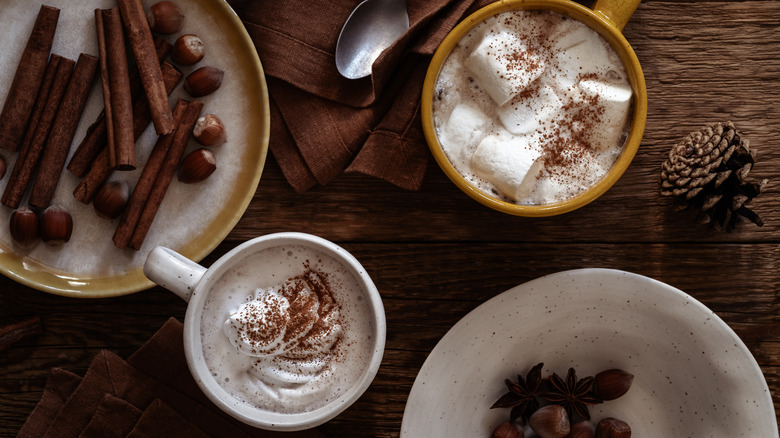 hot chocolate on a table along with cinnamon sticks and nuts