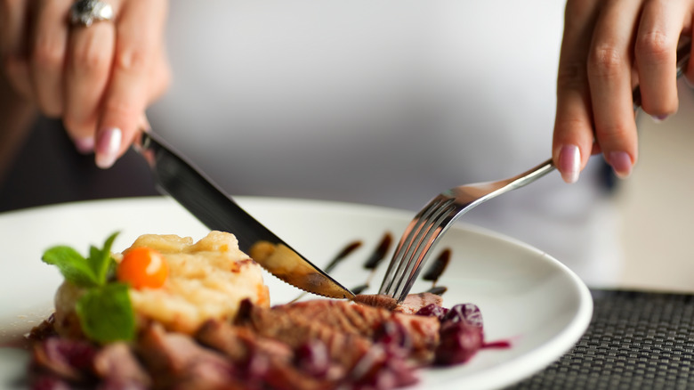 Close-up of woman eating dinner with fork and knife