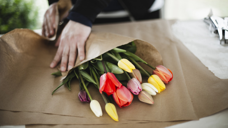 Person wrapping fresh tulips in brown paper