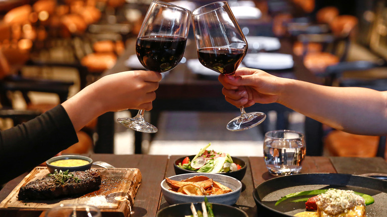 Two people toasting with glasses of red wine over dinner