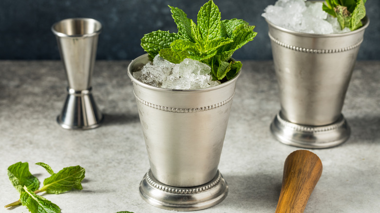 Silver cups filled with ice, mint, and mint julep cocktail