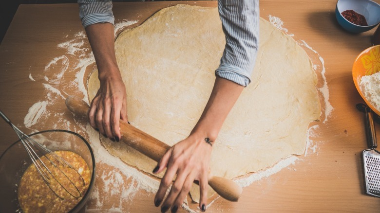 Someone rolling out a circle of dough on a counter