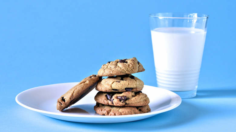 A white plate of chocolate chip cookies next to a clear glass filled with milk