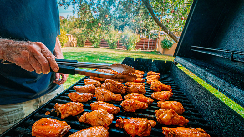 man turning chicken wings on grill