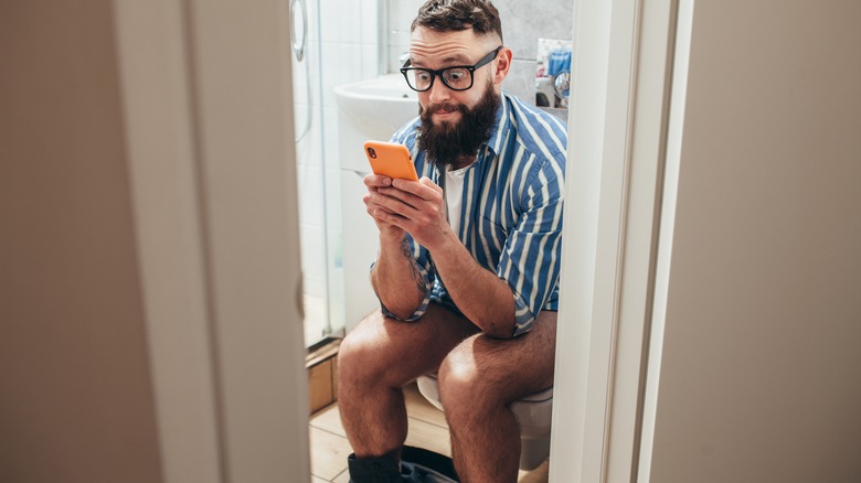 guy sitting on the toilet with his phone