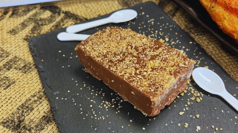 A thick slice of fudge topped with raw sugar has three spoons next to it