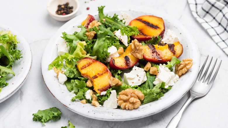 Salad with arugula, grilled peach slices, walnuts, and cheese on white plate