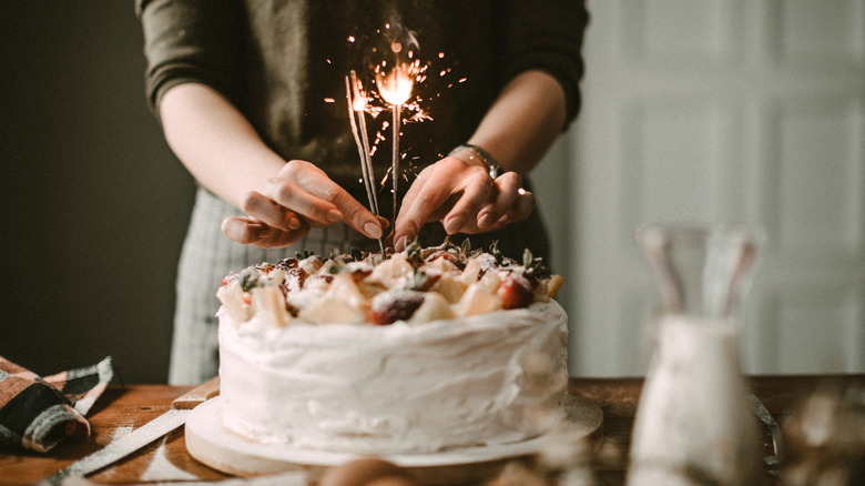 Woman placing sparklers on cake with fruit topping