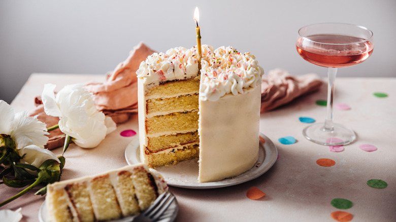 Layered birthday cake with flowers, confetti, and wine