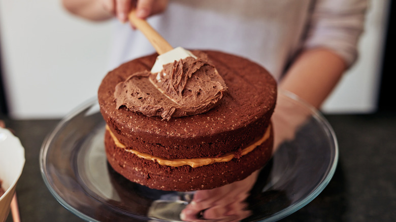 Spreading chocolate icing on a two layer chocolate cake