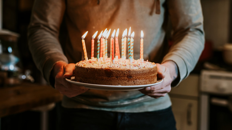 Man holds a birthday cake with many lit candles