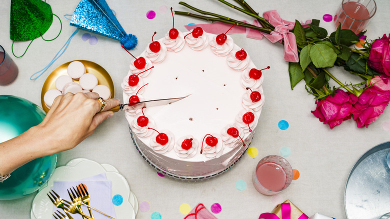 Cutting into a pink party cake decorated with cherries