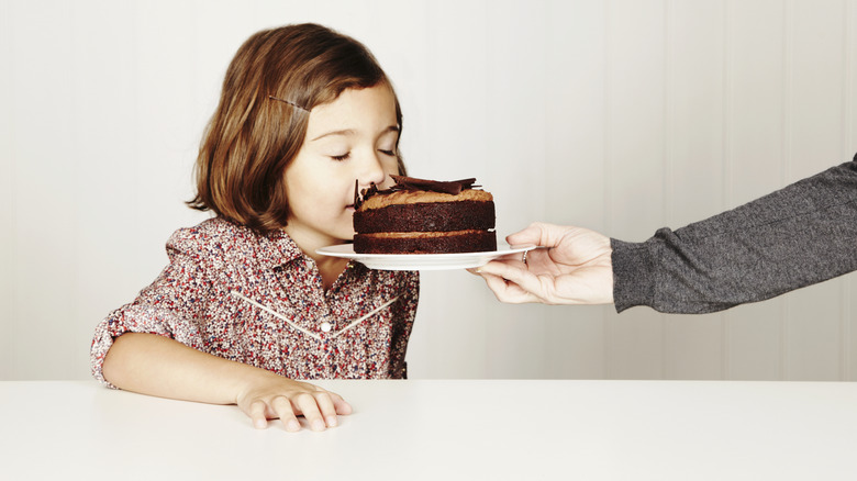 A young girl smells a small chocolate cake with her eyes closed