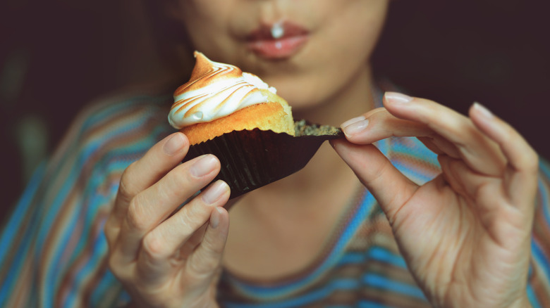 Woman unwraps frosted vanilla cupcake