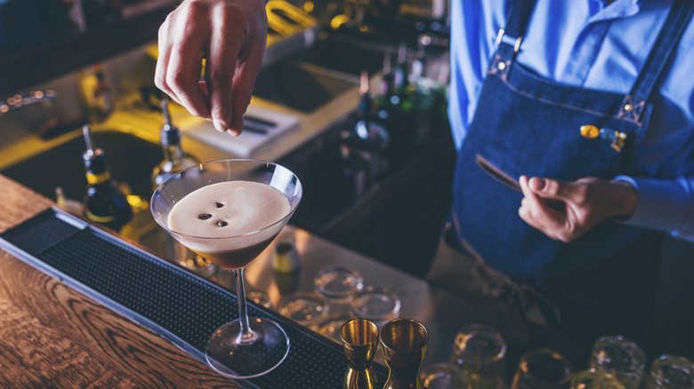 A bartender drops coffee beans as a garnish on an espresso martini