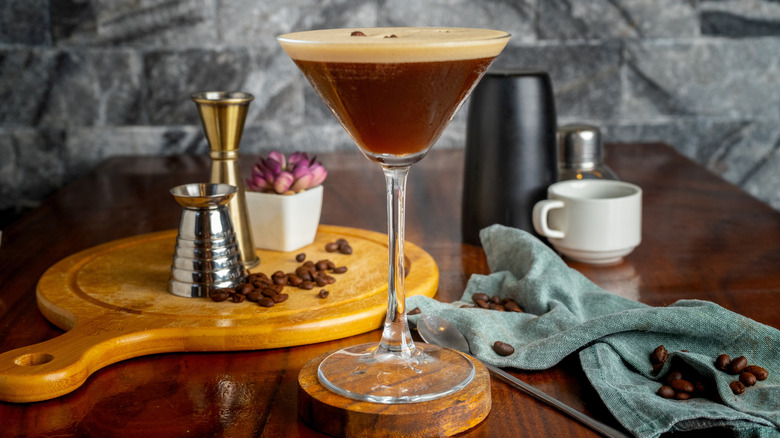 An espresso martini foregrounded on a coffee table with measuring instruments and loose coffee beans