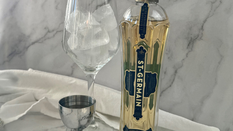 Wine glass with ice next to bottle of St. Germain and jigger