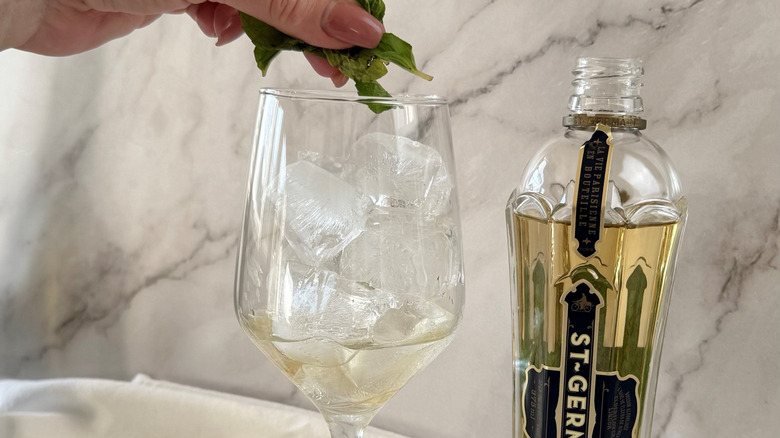 Hand adding fresh mint to wine glass