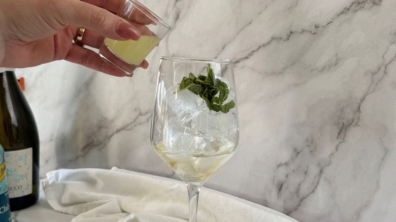 Hand pouring small glass of lime juice into wine glass